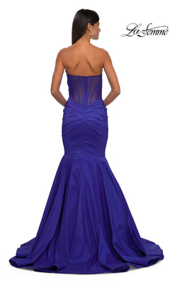 A woman models the La Femme 32791: a strapless long mermaid prom dress in royal blue with a sheer panel back and flared train, showcasing its elegance as she faces away from the camera.