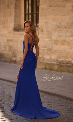 A woman in the floor-length La Femme 32802 prom dress, featuring a lace-up open back, stands on a cobblestone street and looks over her shoulder. "La Femme" is displayed at the bottom right.