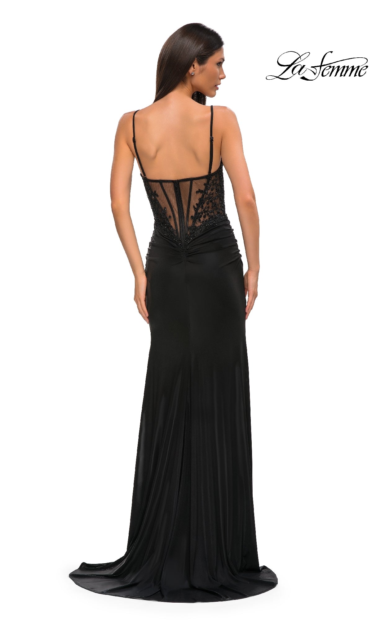 A woman stands with her back to the camera in a black La Femme 32803 Lace-Corset Long Jersey Prom Dress, featuring a sheer lace back, thin straps, fitted silhouette, and slight train for an elegant look.