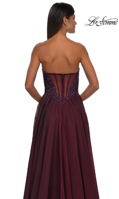 Woman models the Strapless Long A-Line Prom Dress: La Femme 32804 in burgundy, featuring a sheer embroidered back, while facing away; La Femme logo appears in the top right corner.