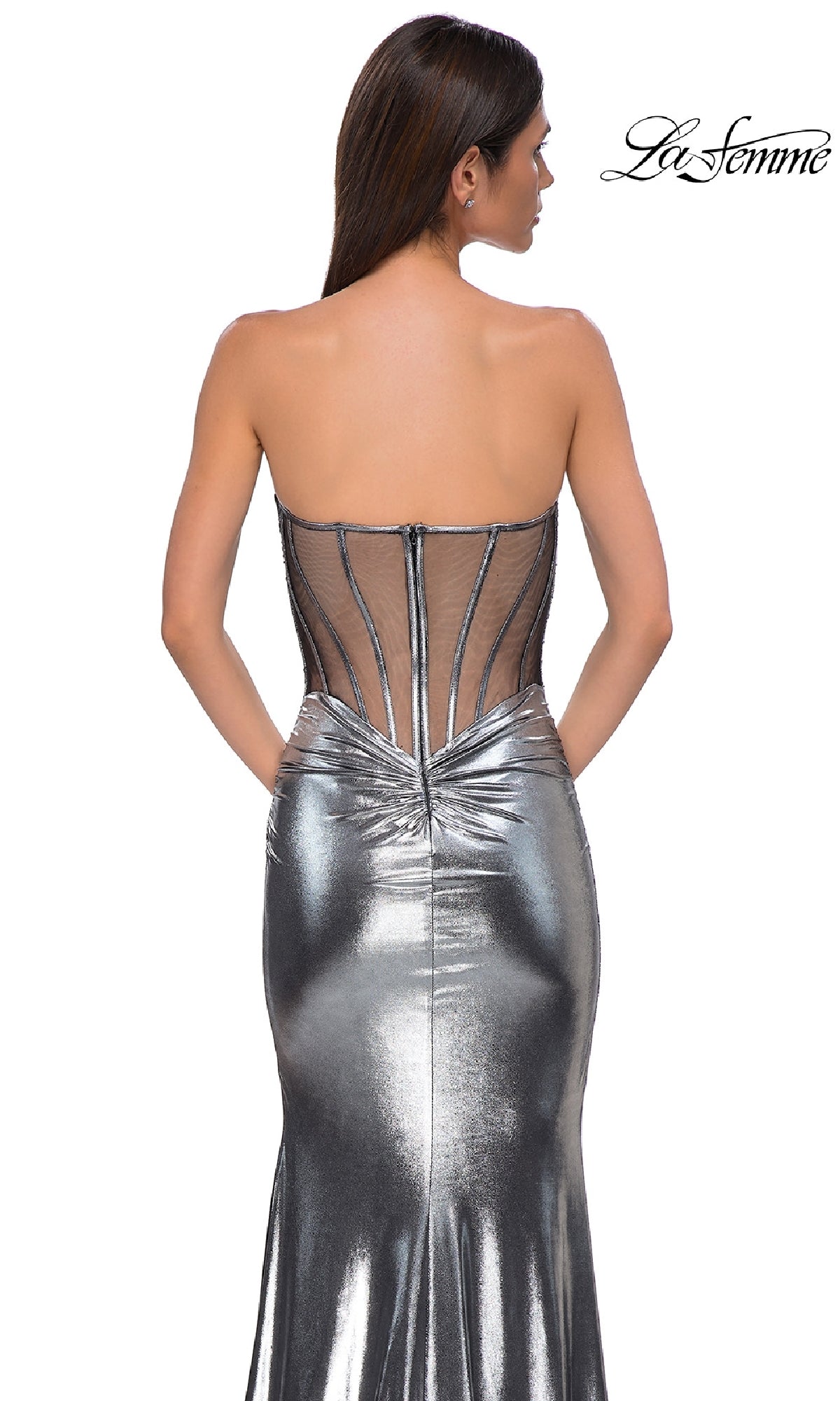 A woman models the Strapless Long Metallic Prom Dress: La Femme 32806, featuring a sheer corset-style back with visible boning, against a white background. The 