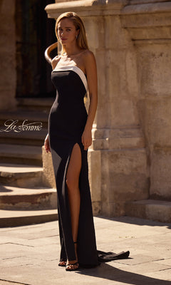 A woman wearing the La Femme 32808 strapless long black prom dress with a mermaid skirt, thigh-high slit, and white side detail stands outdoors on a stone walkway.