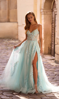 A woman stands on a cobblestone street wearing the La Femme 32810 long prom dress, featuring light blue tulle, beaded lace applique, thin straps, and a high slit.
