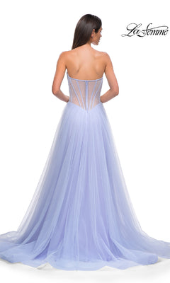 A woman stands with her back to the camera in the Strapless Long Prom Ball Gown: La Femme 32811, featuring a floor-length lavender tulle skirt and a sheer beaded sweetheart corset-style back.