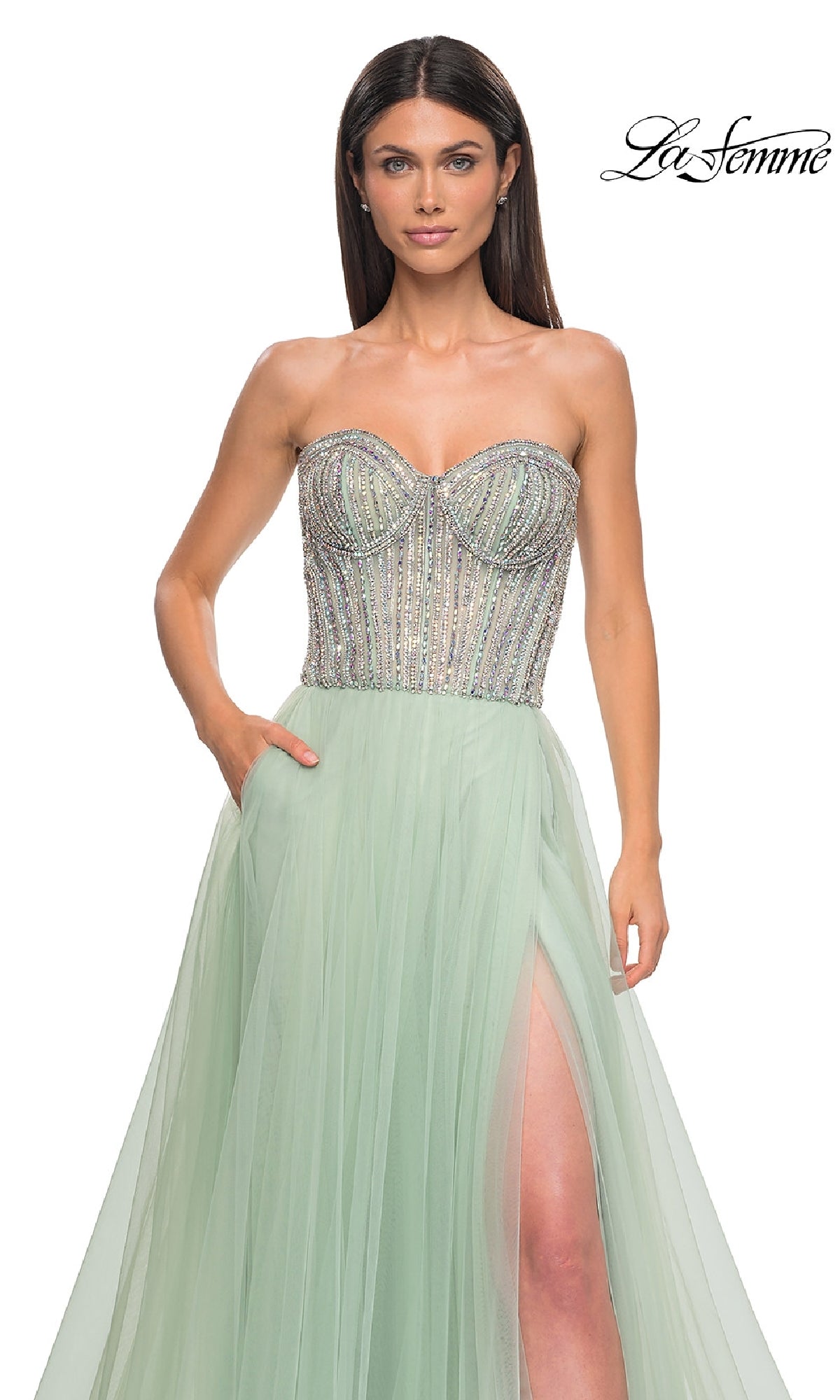 A woman wears the Strapless Long Prom Ball Gown: La Femme 32811, featuring a mint green beaded sweetheart corset bodice and thigh-high slit. The 