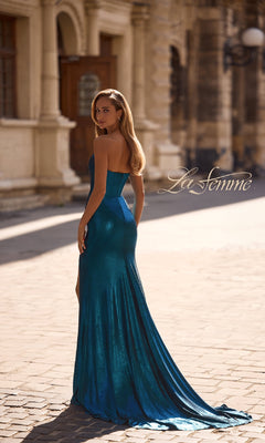 A woman in the La Femme 32828 strapless long metallic prom dress stands on a cobblestone street before a historic building, glancing over her shoulder.