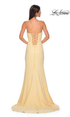 A woman faces away from the camera, wearing the La Femme 32829 lace-up strapless long prom dress in pale yellow.
