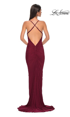 A woman stands facing away, showcasing the Deep V-Back Long Prom Dress: La Femme 32834—a floor-length burgundy gown with crisscross straps, cowl neck, low open back, and slight train—perfect for an elegant prom night.