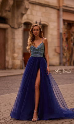 Woman wearing the La Femme 32838 Cowl-Neck Long Indigo Prom Dress, standing on a cobblestone street in front of stone buildings.