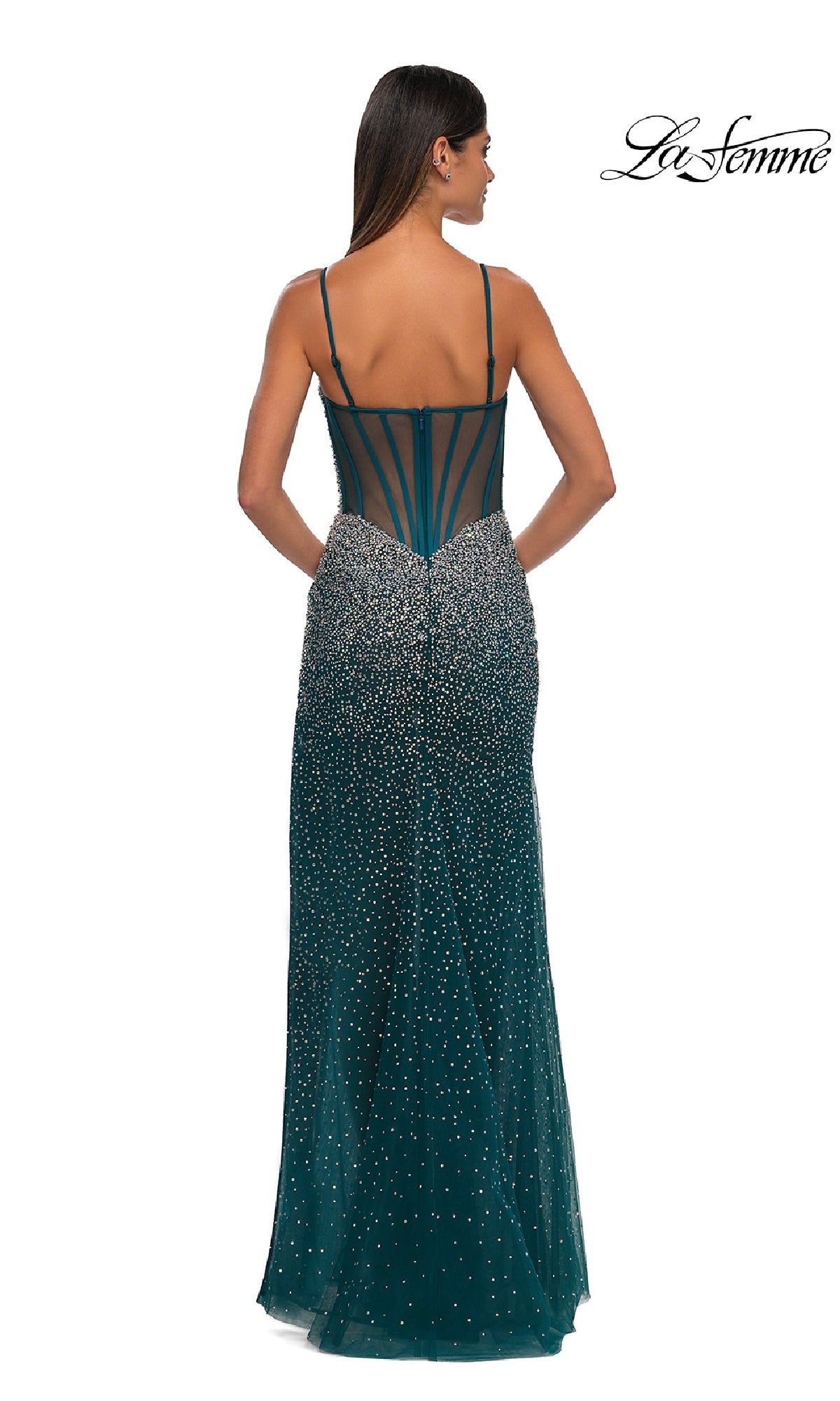 A woman stands with her back to the camera in a sleeveless, emerald green La Femme 32840 long beaded prom dress featuring thin straps, a sheer back panel, and sparkling embellishments.
