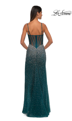 A woman stands with her back to the camera in a sleeveless, emerald green La Femme 32840 long beaded prom dress featuring thin straps, a sheer back panel, and sparkling embellishments.