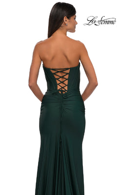 Woman wearing the Strapless Sweetheart Prom Gown: La Femme 32843 in dark green, featuring a lace-up corset back, stands facing away from the camera against a white background.