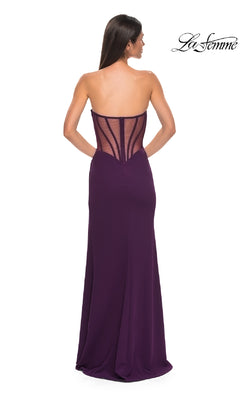 A woman wears the Asymmetrical Strapless Prom Gown: La Femme 32849 in purple, featuring a sheer corset-style back. She stands facing away, with the "La Femme" logo displayed in the upper right corner to showcase this elegant gown.