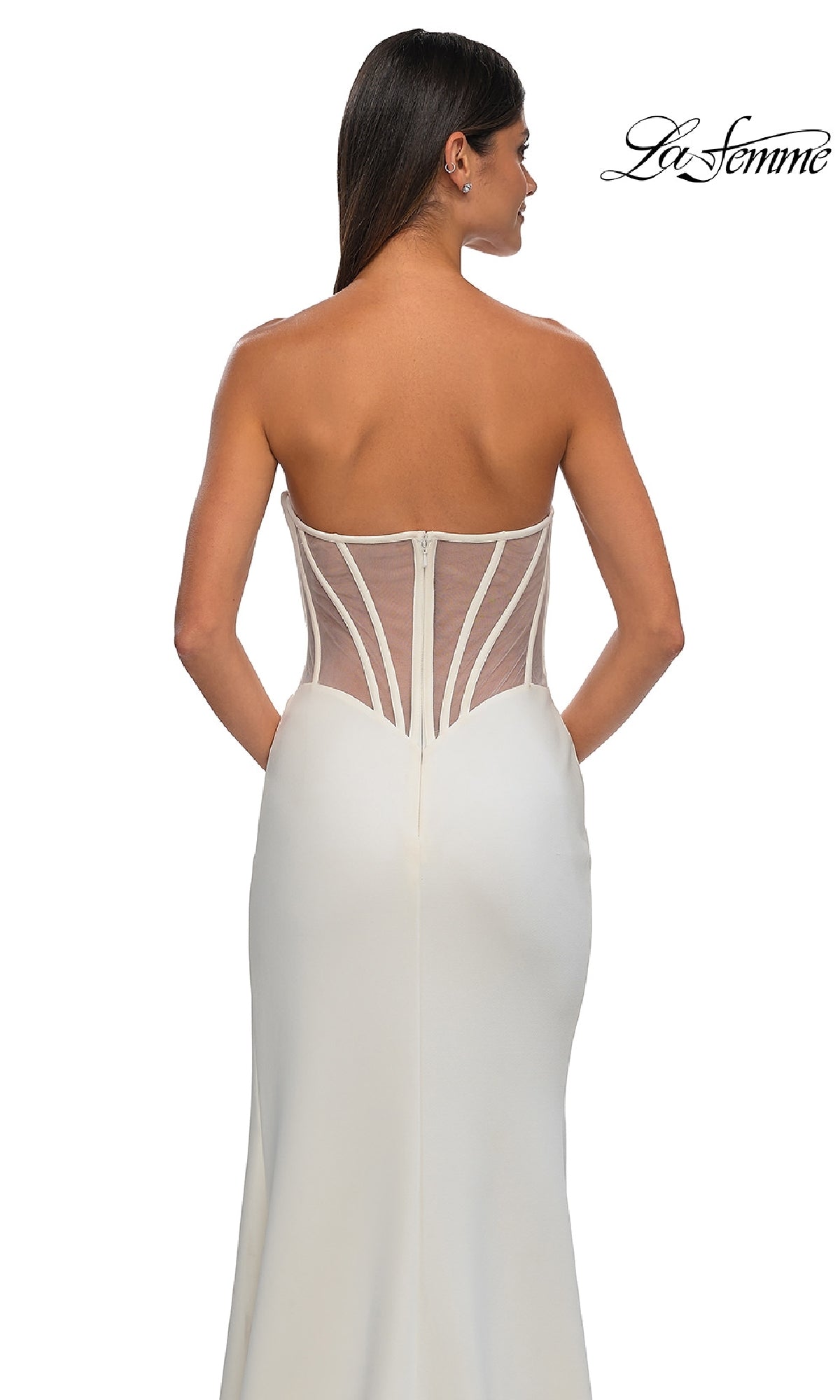 A woman models the Asymmetrical Strapless Prom Gown: La Femme 32849, featuring a sheer structured back panel. The long, strapless dress fits closely through the waist and hips, creating an elegant silhouette as she faces away from the camera.