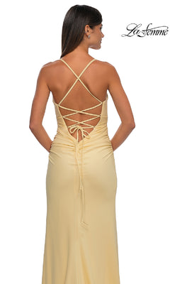 A woman stands with her back to the camera wearing the Strappy-Back Long Prom Dress La Femme 32851 in light yellow, featuring a lace-up open back and thin crisscross straps.