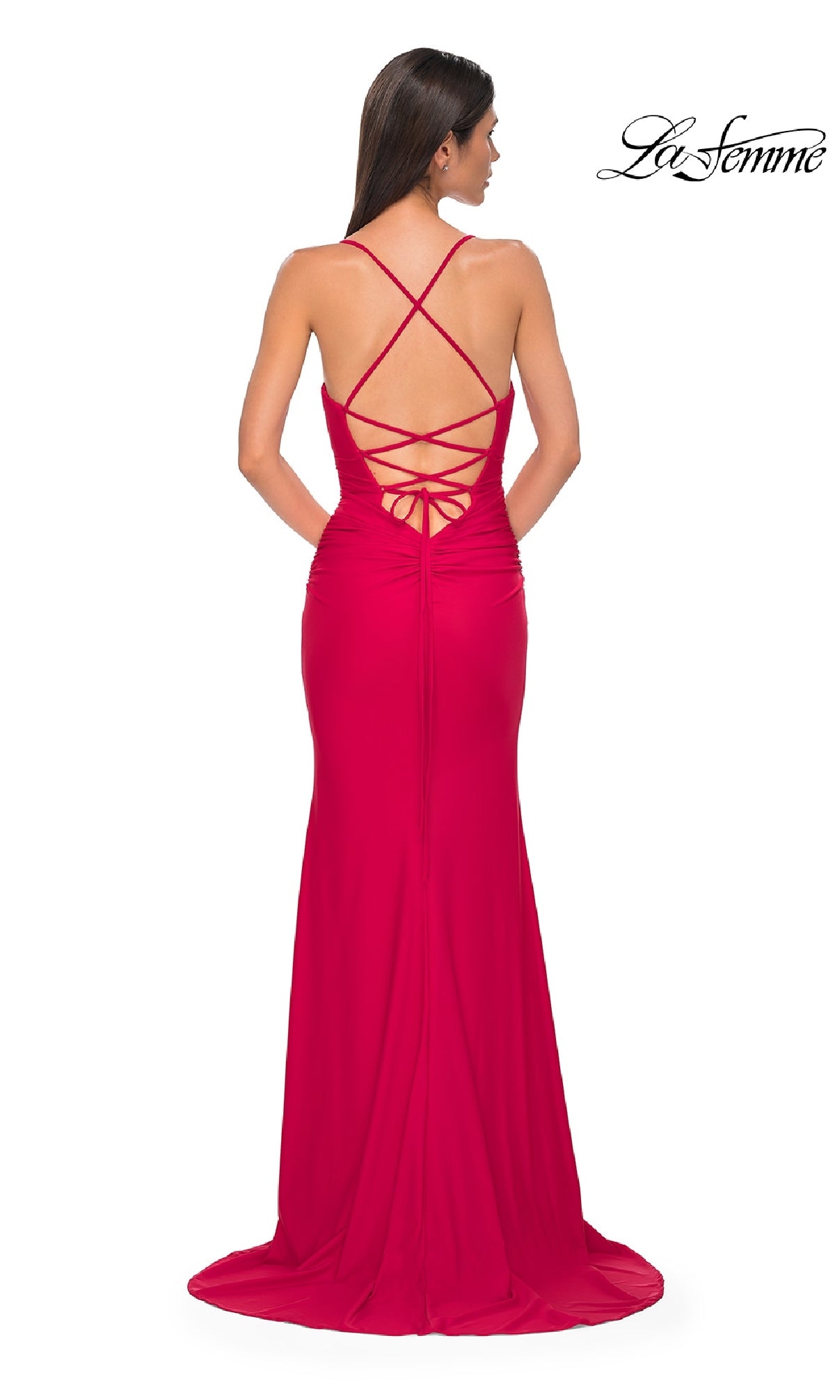 A woman stands facing away, wearing the Strappy-Back Long Prom Dress: La Femme 32851, featuring floor-length style with crisscross straps and a lace-up back.