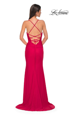 A woman stands facing away, wearing the Strappy-Back Long Prom Dress: La Femme 32851, featuring floor-length style with crisscross straps and a lace-up back.