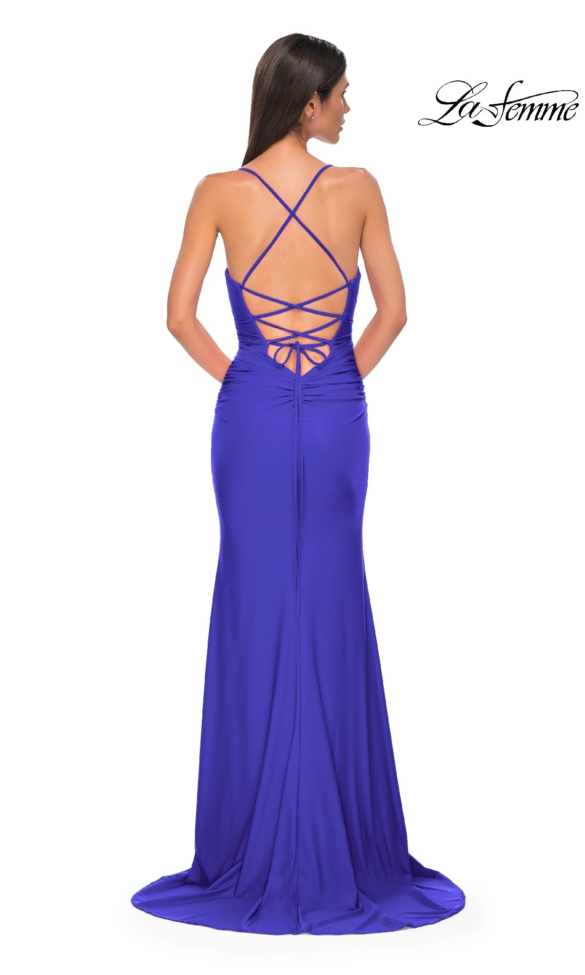 A woman stands facing away in a floor-length royal blue Strappy-Back Long Prom Dress: La Femme 32851, featuring a crisscross lace-up open back design.