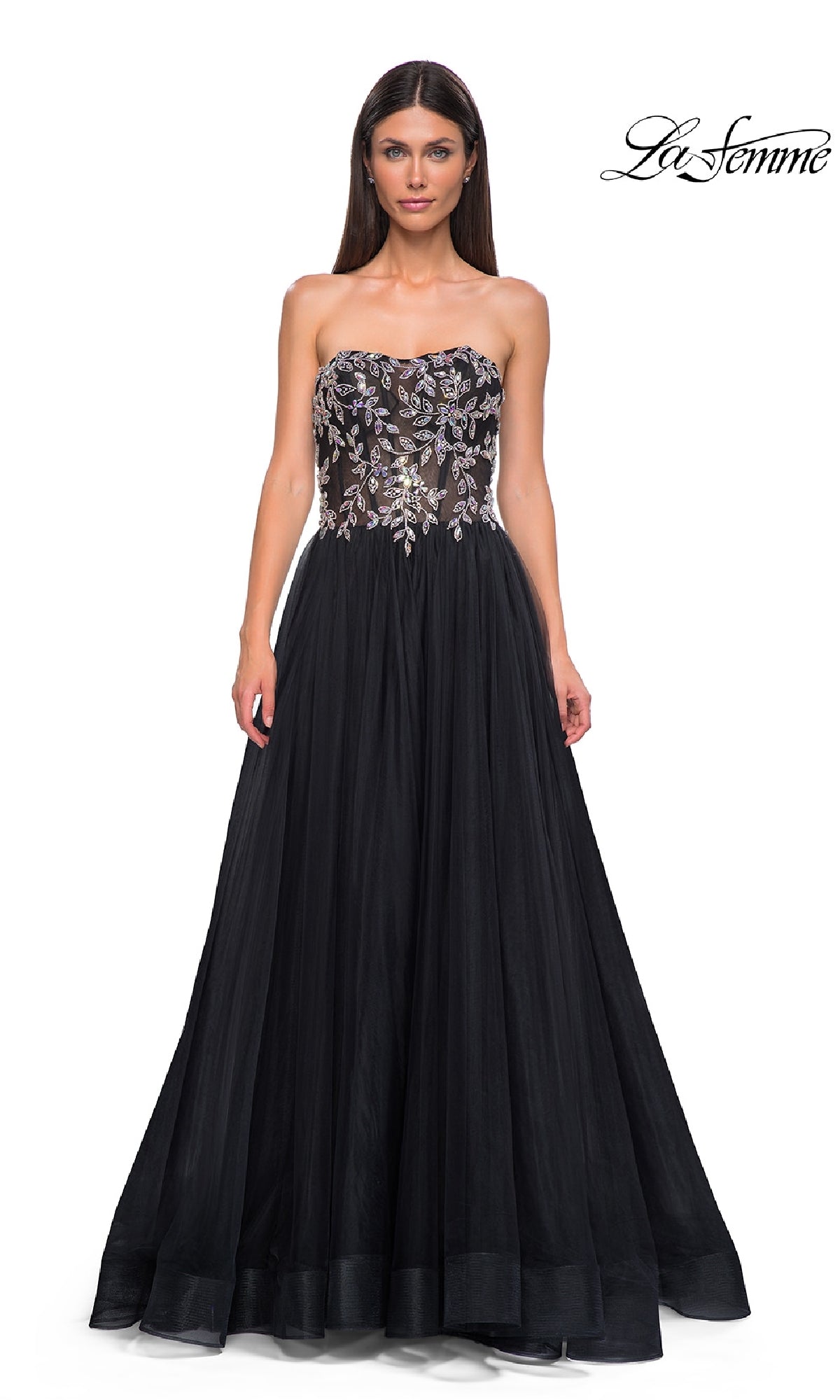 A woman wears the Beaded-Corset Strapless Prom Gown: La Femme 32862, featuring a sheer, floral-embellished bodice and flowing tulle skirt. The 