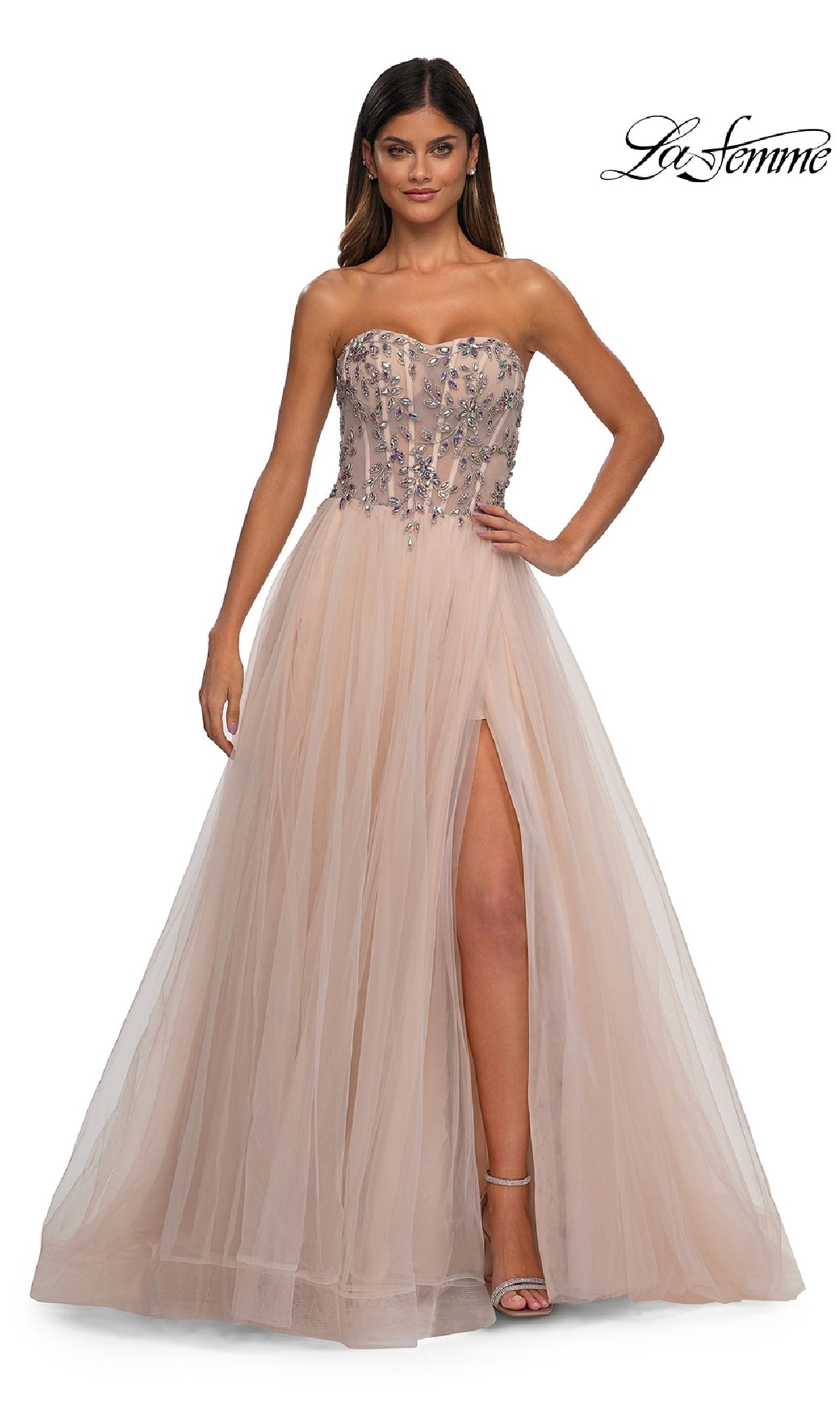 A woman poses elegantly in the Beaded-Corset Strapless Prom Gown: La Femme 32862—blush tulle with a beaded corset bodice, floral accents, and a thigh-high slit—against a white background.