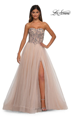 A woman poses elegantly in the Beaded-Corset Strapless Prom Gown: La Femme 32862—blush tulle with a beaded corset bodice, floral accents, and a thigh-high slit—against a white background.