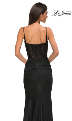 A woman stands with her back to the camera in the Lace-Bodice Long Black Prom Dress, La Femme 32873, featuring lace detailing on the back and thin straps.
