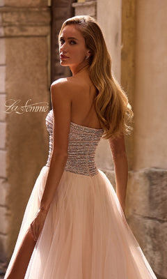 A woman in the Strapless Long Prom Ball Gown: La Femme 32875, featuring beaded embellishments and a tulle skirt, stands outdoors looking over her shoulder.