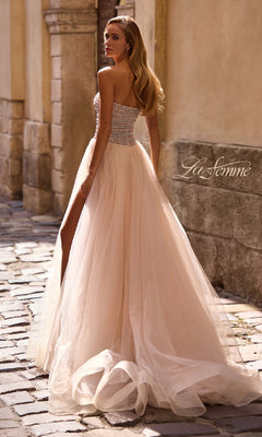 A woman wearing the La Femme 32875 Strapless Long Prom Ball Gown with beaded details and a high slit stands on a cobblestone street, glancing over her shoulder.