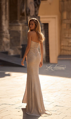 A woman in the Bodycon Long Metallic Prom Dress: La Femme 32876, featuring a sweetheart neckline, poses outdoors before a sunlit stone building. "La Femme" is displayed in the image.