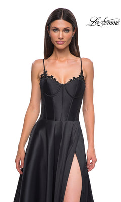 A woman models the Lace-Up Long Mikado Prom Dress (La Femme 32878), a black satin gown with thin straps, lace bodice detail, and a thigh-high slit, posed against a white background with the "La Femme" logo.