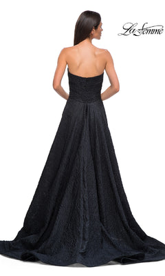A woman with long dark hair models the La Femme 32893, a textured strapless black prom dress with a full a-line skirt. The photo is taken from the back, displaying the La Femme logo in the corner.
