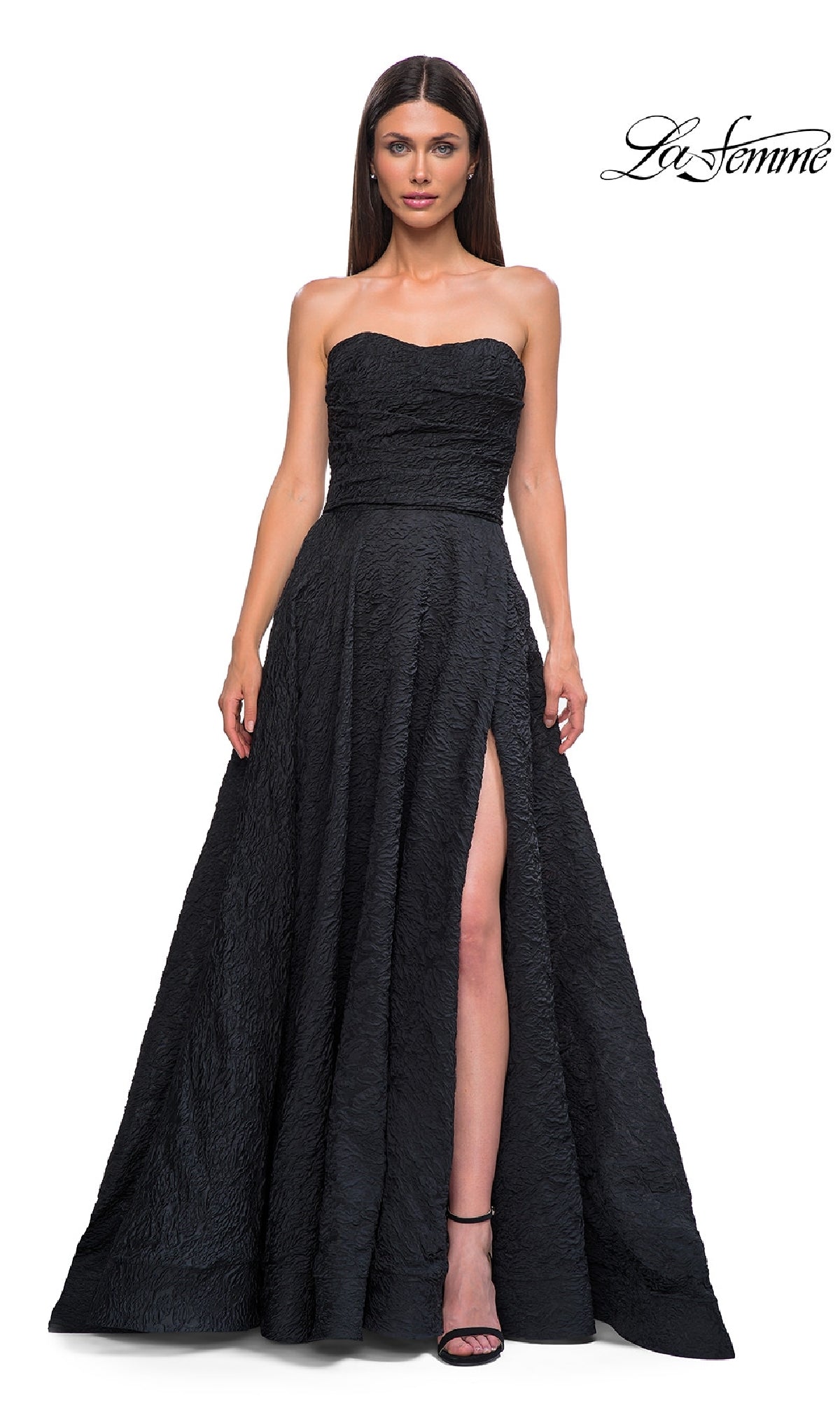 Woman modeling the La Femme 32893 textured strapless black prom dress with a thigh-high slit, posed against a white background; 