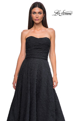 A woman in the La Femme 32893 textured strapless black prom dress with a full skirt stands against a white background. The La Femme logo appears in the top right corner.