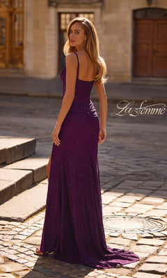 A woman in a fitted, purple Sheer-Waist Long Beaded Prom Dress (La Femme 32947) stands outdoors on a cobblestone street, looking over her shoulder and exuding elegance.