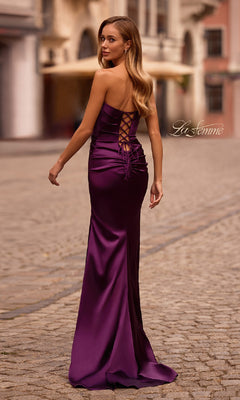 Wearing the La Femme 32952 Strapless Long Satin Prom Dress with a lace-up back, a woman stands on a cobblestone street, glancing over her shoulder.