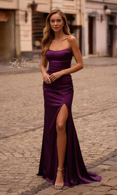 A woman in the Strapless Long Satin Prom Dress: La Femme 32952, featuring a thigh-high slit, stands elegantly on a cobblestone street.