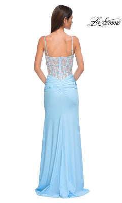 A woman stands with her back to the camera wearing the La Femme 32957 light blue prom dress, featuring a floor-length skirt, lace-up sheer back, spaghetti straps, and a sheer corset bodice.