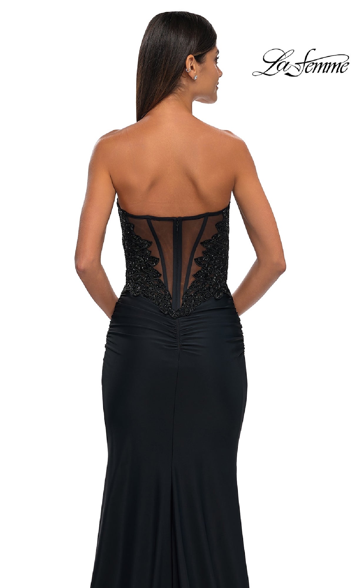 Woman in the Strapless Sweetheart Prom Gown: La Femme 32961, featuring a sheer back panel and black sequin embellishments, stands with her back to the camera.