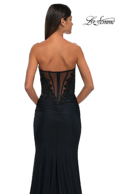 Woman in the Strapless Sweetheart Prom Gown: La Femme 32961, featuring a sheer back panel and black sequin embellishments, stands with her back to the camera.