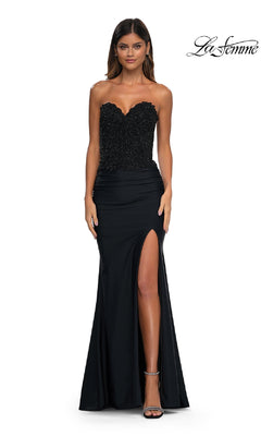 A woman in the Strapless Sweetheart Prom Gown: La Femme 32961, with a beaded corset bodice and high slit, poses elegantly against a white background.