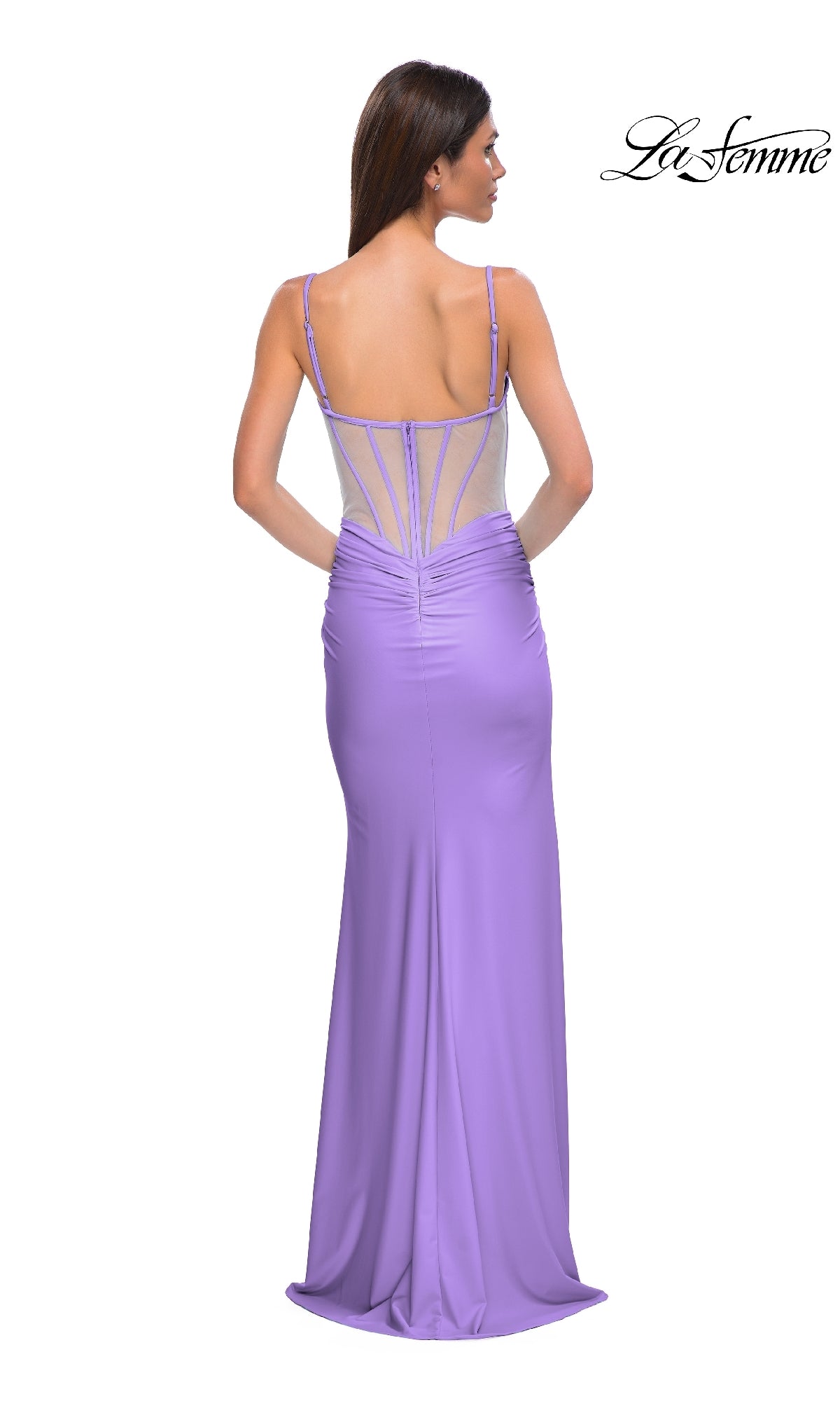 A woman stands with her back to the camera in the Long Jersey Corset Prom Dress: La Femme 32962, a floor-length lilac gown featuring a mesh back, thin straps, and a fitted corset bodice. The 