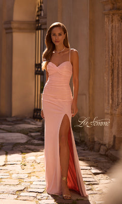 A woman in the La Femme 32964 long prom dress—light pink, sleeveless, with a sweetheart neckline and thigh-high slit—stands on a cobblestone path beside a stone building.