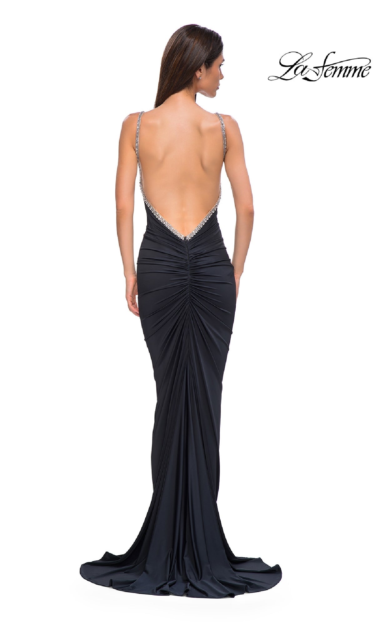A woman models the La Femme 32970 Backless Ruched Long Prom Dress in black, featuring rhinestone straps, a dramatic open back, elegant ruched details, and a subtle train as she faces away from the camera.