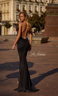 A woman stands outdoors on a city street, looking over her shoulder in the Backless Ruched Long Prom Dress: La Femme 32970.