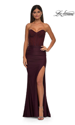 A woman models the Strapless Long Corset Prom Dress: La Femme 32971, featuring a burgundy hue, sheer corset bodice, lace-up back, and high slit, standing against a white background with "La Femme" branding in the corner.