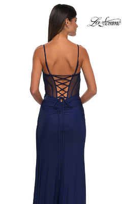 A woman wears the La Femme 32977 Side-Sash Lace-Up Long Prom Dress in navy, featuring thin straps and a sheer mesh back, while standing turned away. The La Femme logo appears in the top right corner.