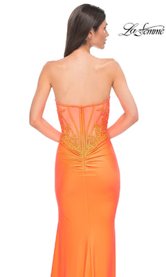 A woman stands with her back to the camera, wearing the Beaded-Bodice Long Prom Dress La Femme 32981 in orange, featuring a strapless design, sheer embroidered back panels, and delicate beaded accents.