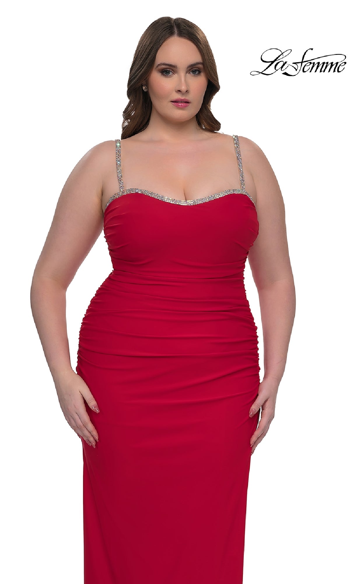 A woman wears the Plus-Size Long Prom Dress: La Femme 32992, a sleeveless fitted red gown with rhinestone straps and ruched details, standing against a white background. The 