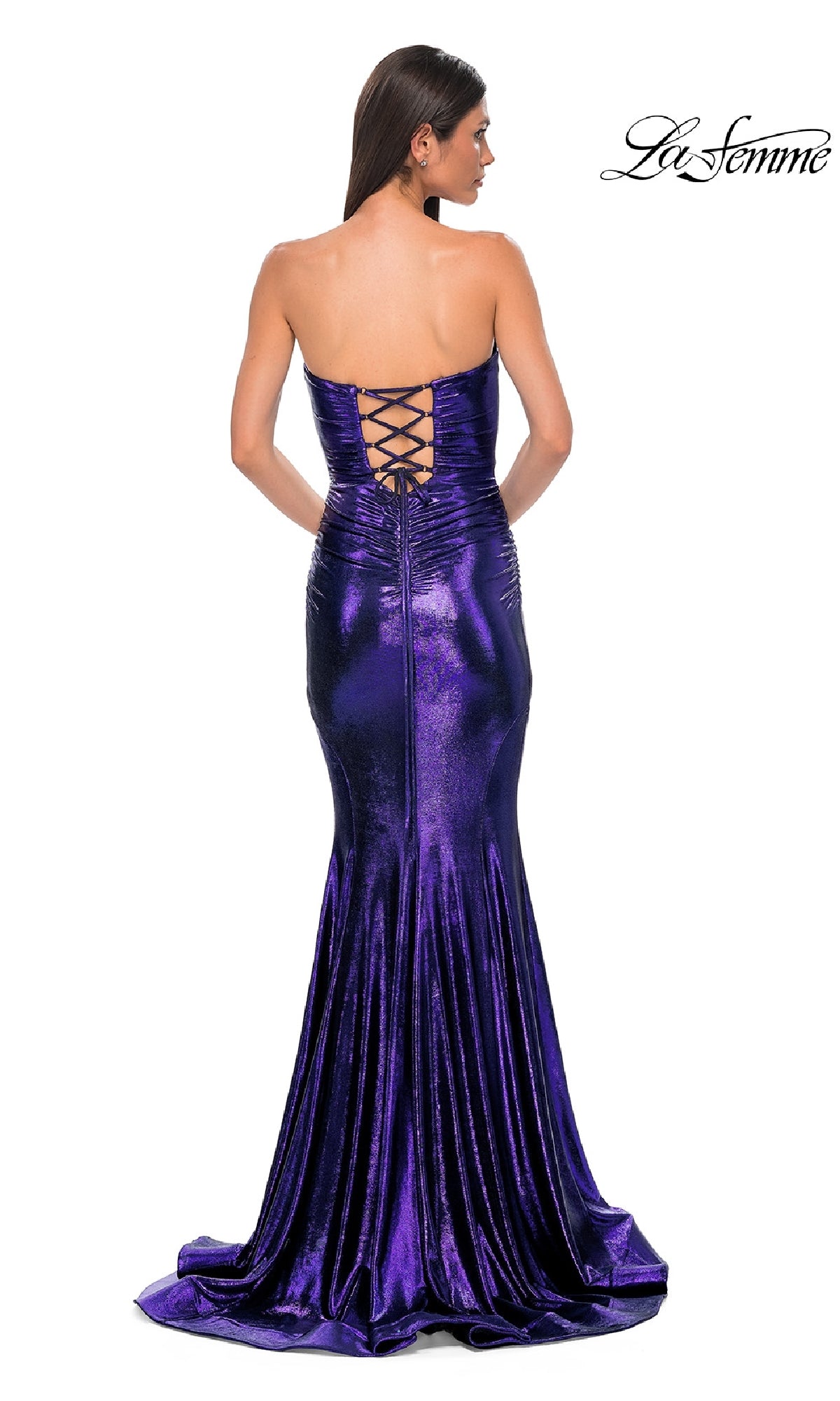 A woman wears the Strapless Long Metallic Prom Dress: La Femme 32995, a metallic purple mermaid gown with a strapless neckline and lace-up back, standing against a white background.