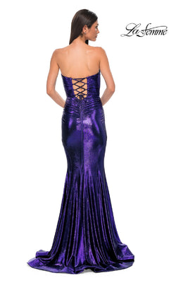 A woman wears the Strapless Long Metallic Prom Dress: La Femme 32995, a metallic purple mermaid gown with a strapless neckline and lace-up back, standing against a white background.